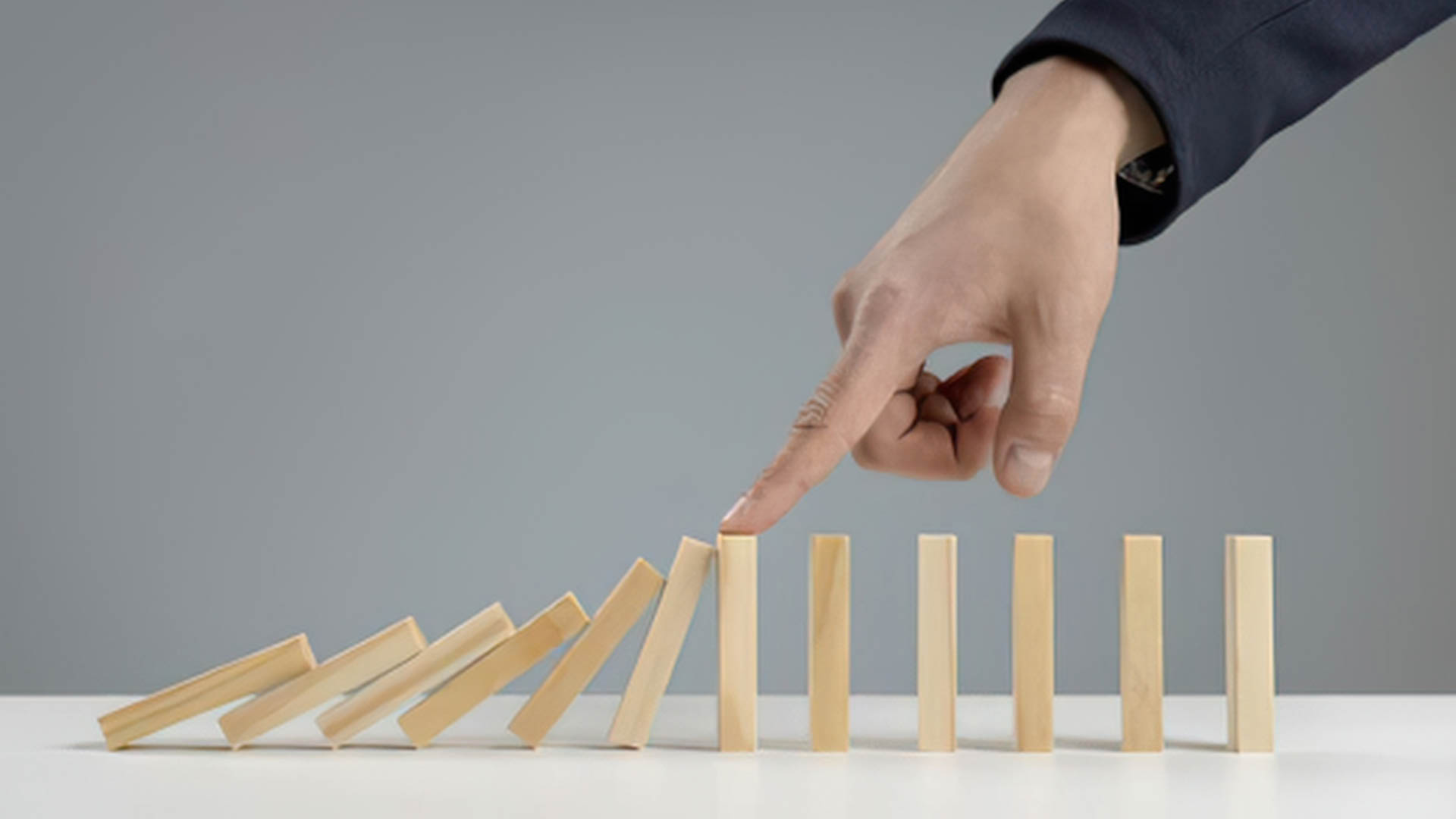 Hand stopping falling wooden blocks, symbolizing preventing failure or maintaining momentum.