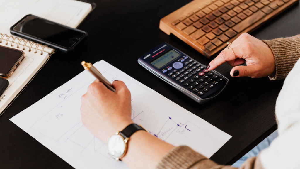 Desk workspace with calculator, smartphone, and notebook used for budgeting and calculations.