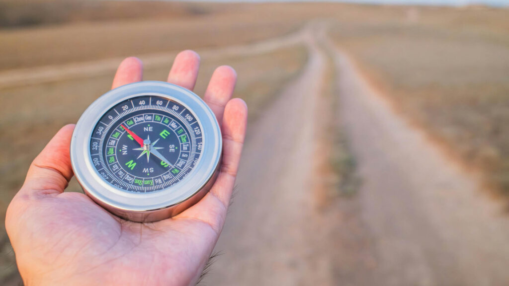 Hand holding a compass on a dirt road symbolizing direction and decision-making in business.