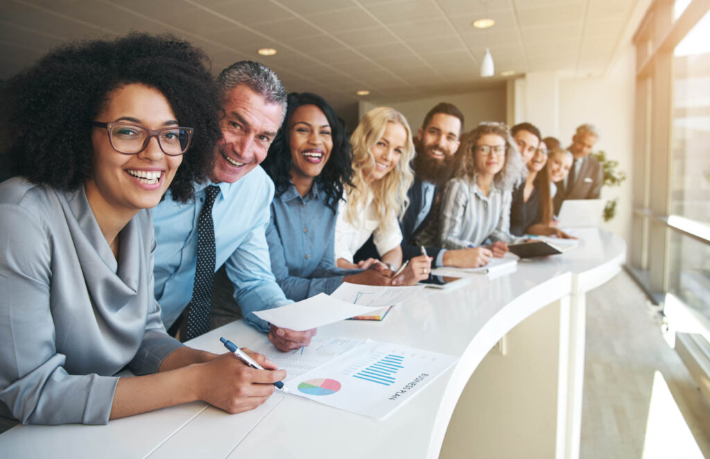 Diverse team of business professionals smiling and collaborating at a conference table with charts and documents.