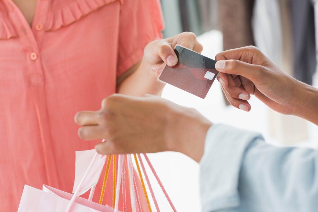 Closeup mid section of female customer receiving shopping bags and credit card from saleswoman in boutique